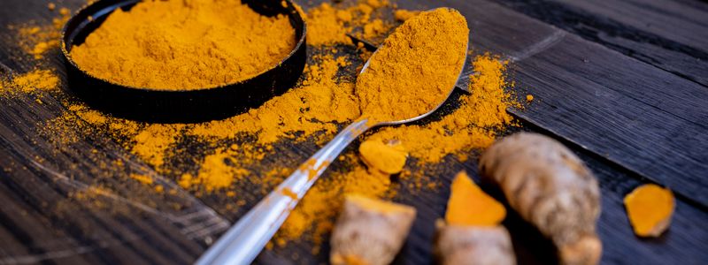 Turmeric powder in a bowl and on a spoon beside fresh turmeric root on a dark surface