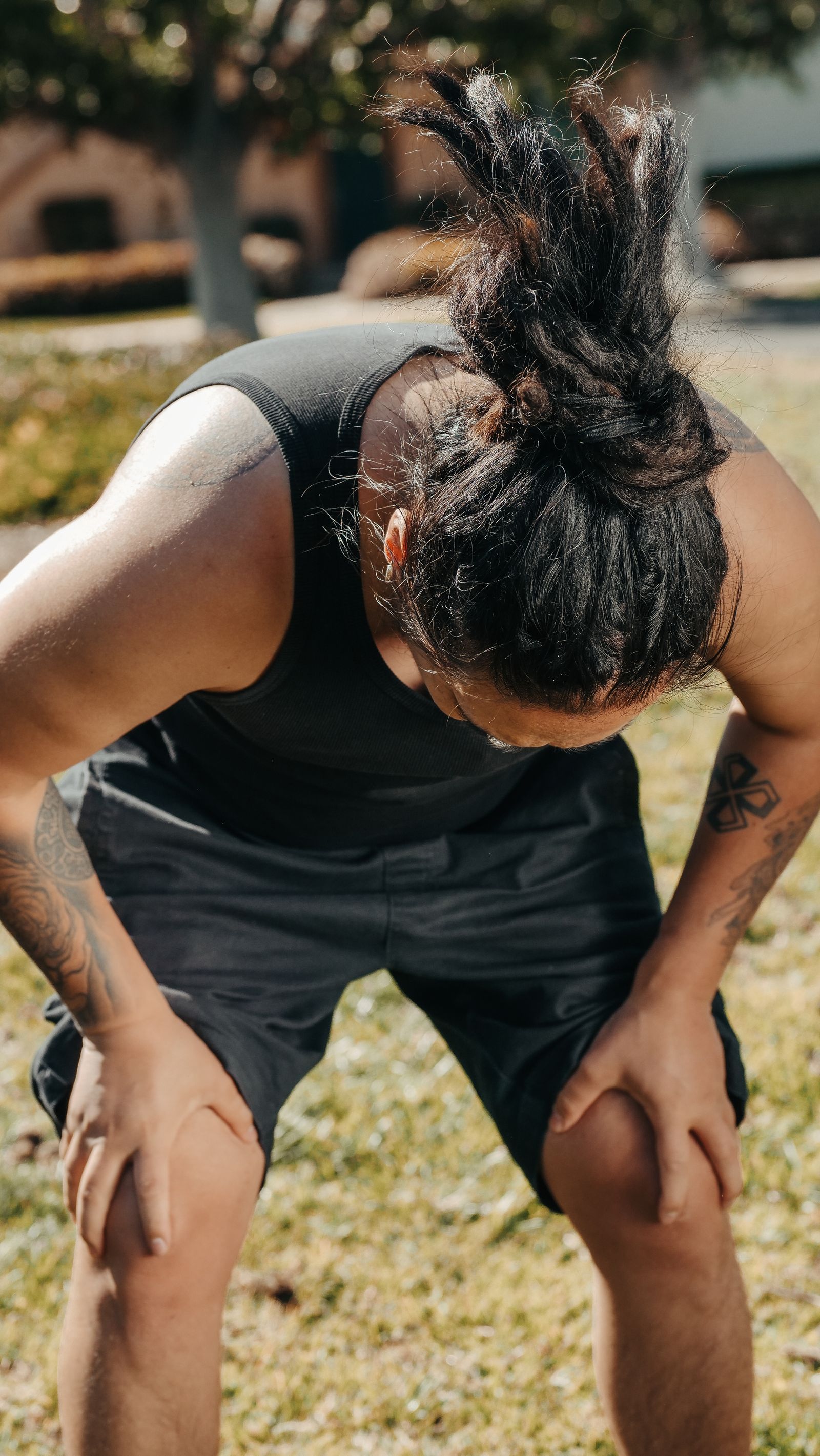 An adult pausing outdoors with hands resting on both knees after exercise