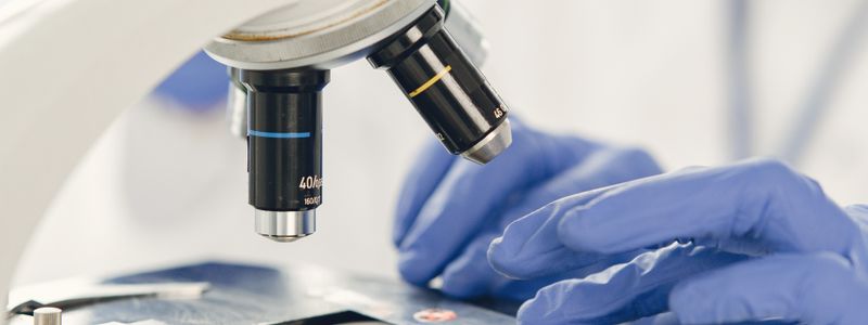 A gloved researcher placing a specimen slide under a laboratory microscope