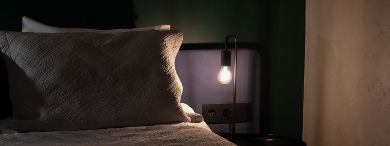 A dim bedroom at night with a warm bedside lamp glowing beside a pillow