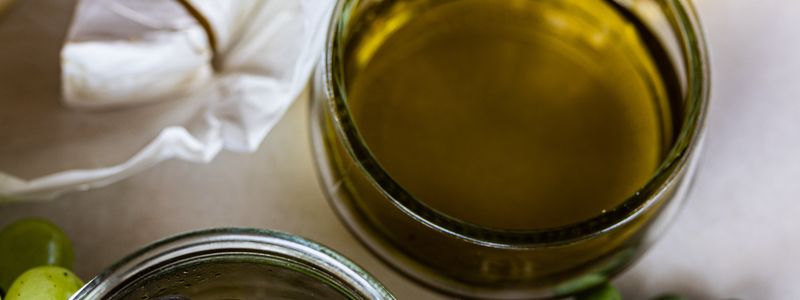 A jar of golden olive oil beside a bowl of olives, cheese and bread in a Mediterranean spread