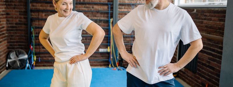 An older man and woman lifting light weights together in a gym
