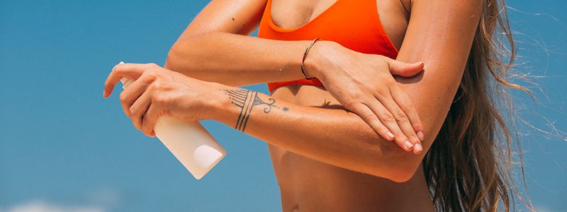 A woman applying sunscreen to her skin outdoors on a sunny day