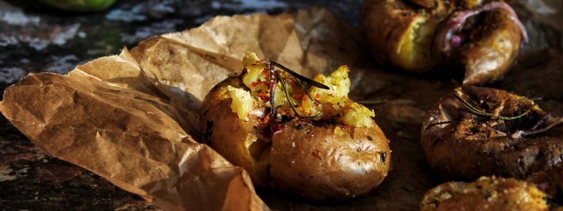 Baked potatoes split open in their skins on brown paper