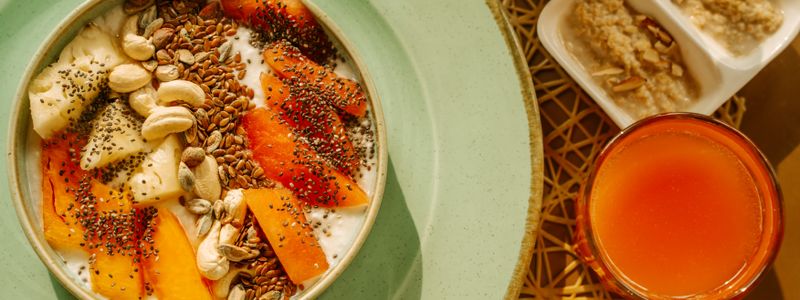A breakfast bowl topped with nuts and seeds beside a glass of juice
