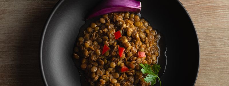 Cooked lentils in a dark pan with red pepper and fresh parsley