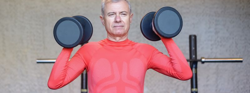 Man in his 60s pressing two dumbbells at shoulder height