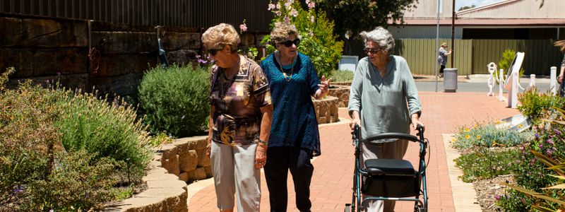 Three older adults walking together outdoors on a garden path