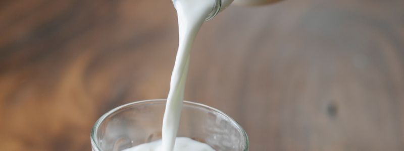 Kefir being poured from a bottle into a clear drinking glass