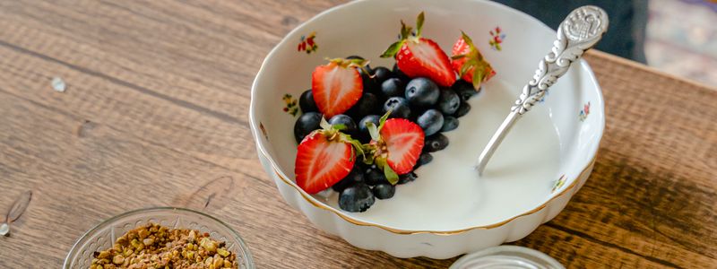 A white bowl of plain yogurt topped with strawberries and blueberries beside a dish of granola