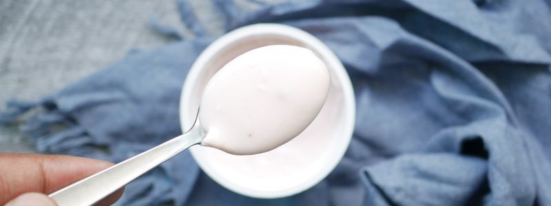 A spoonful of plain yogurt held above a white bowl