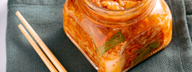 Kimchi in a clear glass jar beside wooden chopsticks