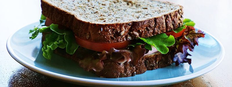 A sandwich made with whole-grain seeded bread, lettuce, and tomato on a plate