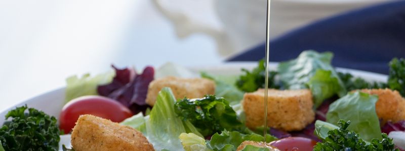Extra-virgin olive oil being poured over a fresh green salad