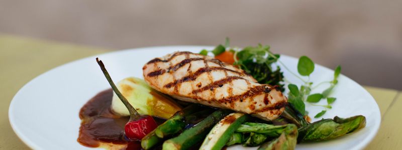 Grilled chicken breast with grilled vegetables on a white plate