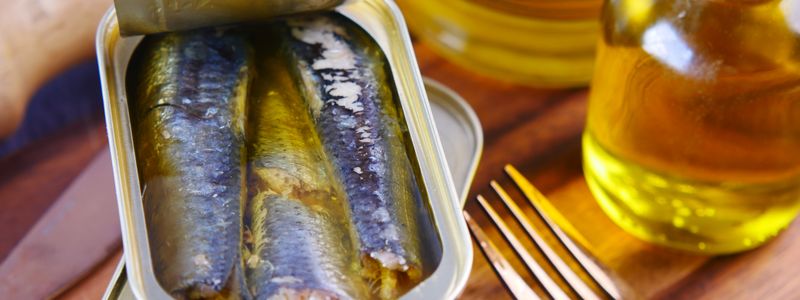 Open tin of sardines on a wooden board