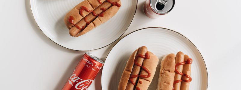 Hot dogs on a plate beside cans of cola
