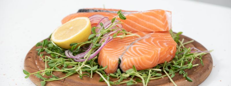 Fresh salmon fillets with a lemon slice and microgreens on a wooden board