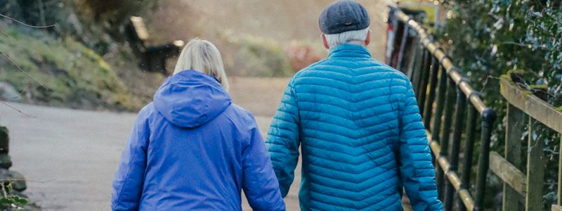 An older couple walking together outdoors on a park path