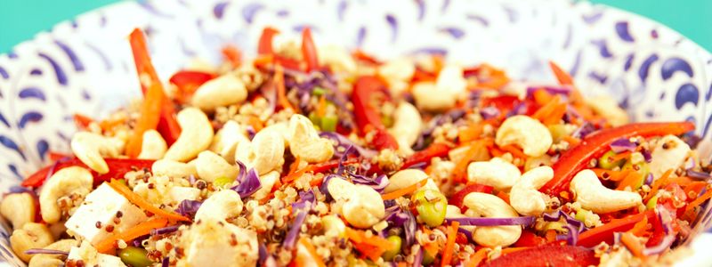 A whole-grain quinoa salad bowl with peppers, carrots, red cabbage, and cashews