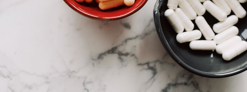 White supplement capsules in small bowls on a marble surface