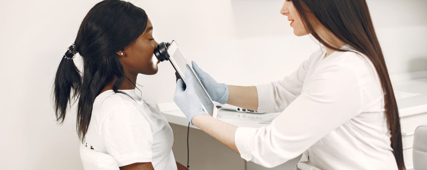 A dermatologist examines a woman's facial skin with a handheld dermatoscope in a clinic