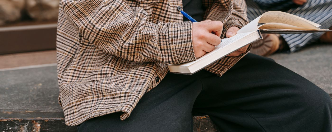 Person sitting outdoors writing in a lined notebook with a pen