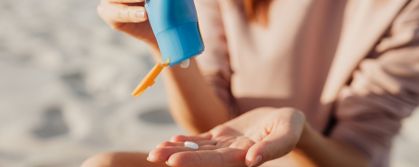 A person applies sunscreen at the beach on a sunny day