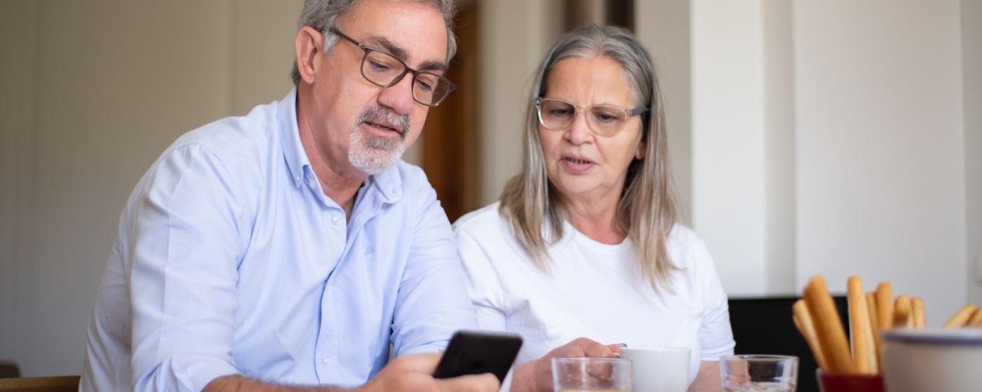 An elderly couple enjoys breakfast together, using a smartphone