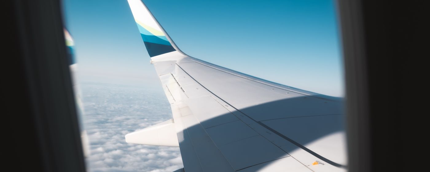 View of an aircraft wing and clouds through a passenger window seat