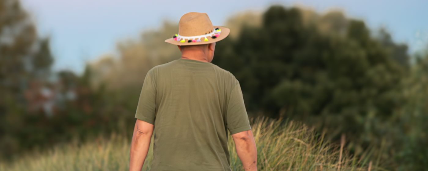 A man in a sun hat walking away from the camera along a grassy path