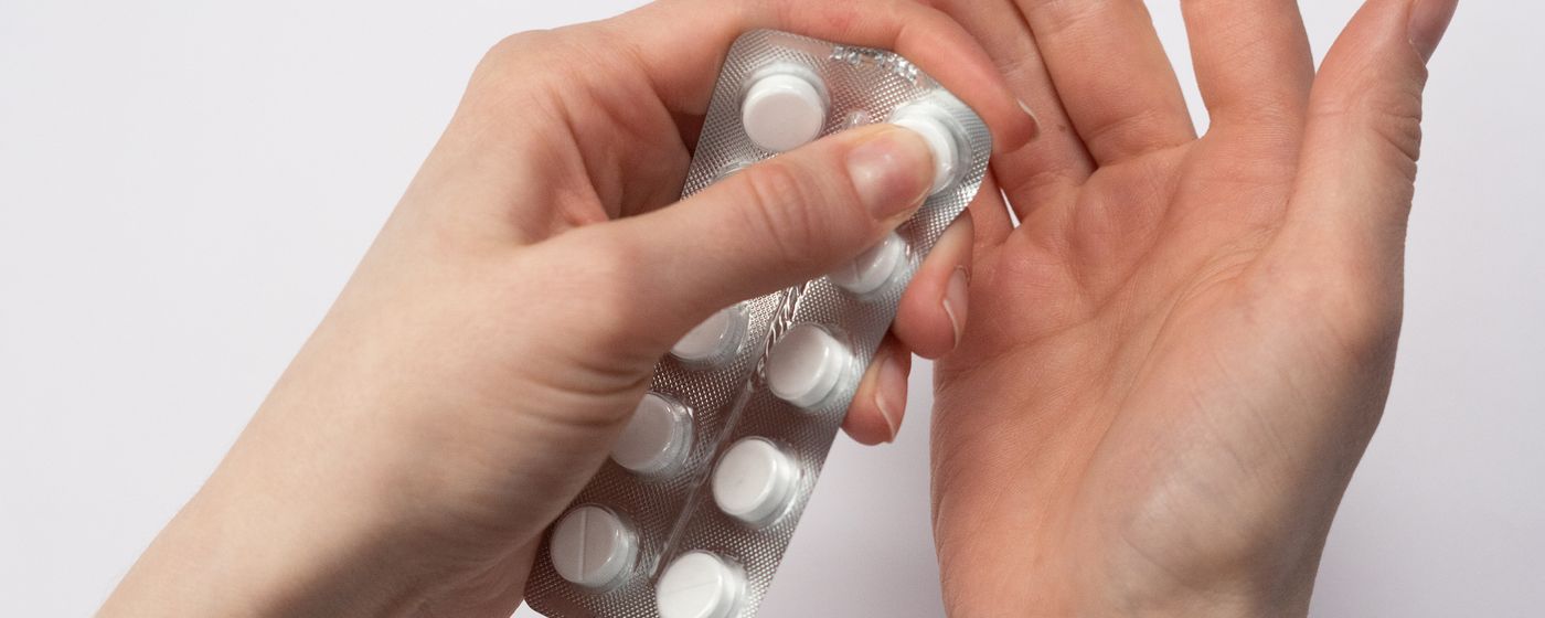 Two hands holding a blister pack of white tablets