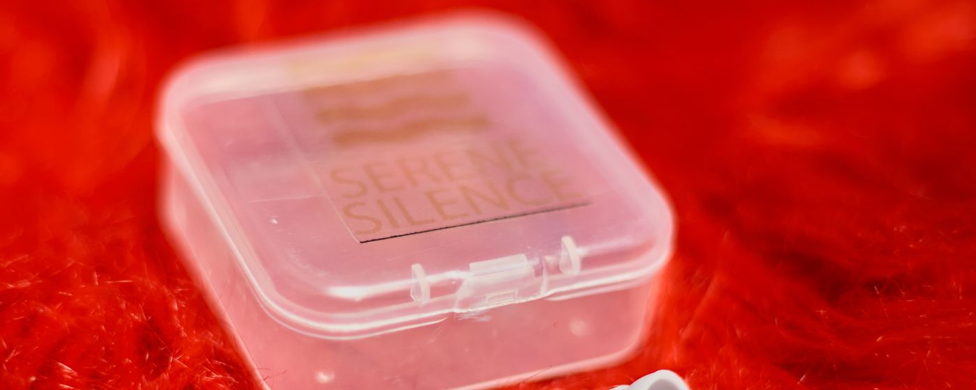 A small clear case of foam earplugs on a red surface