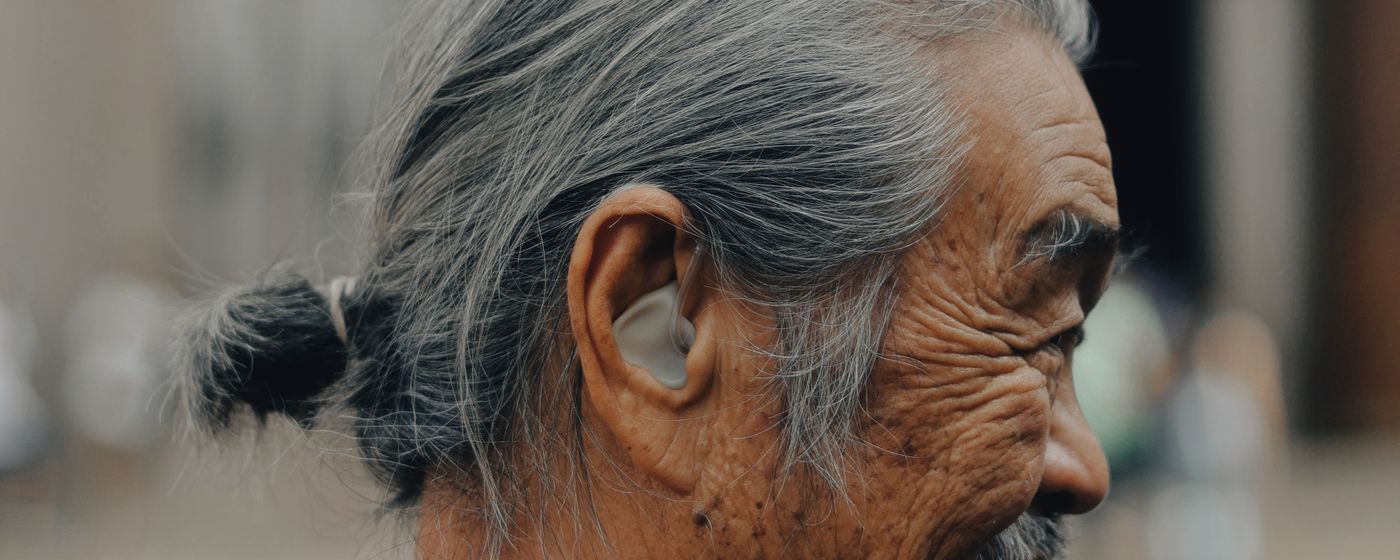 An older adult photographed in profile with a hearing aid visible in the ear