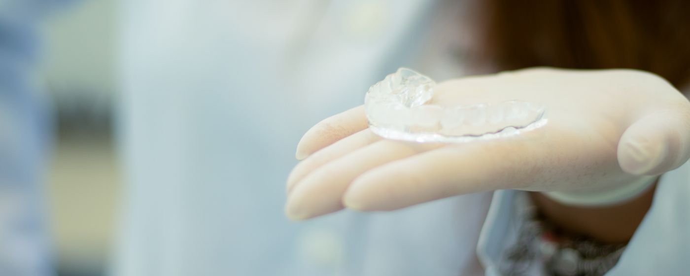A gloved hand holding a clear moulded dental appliance