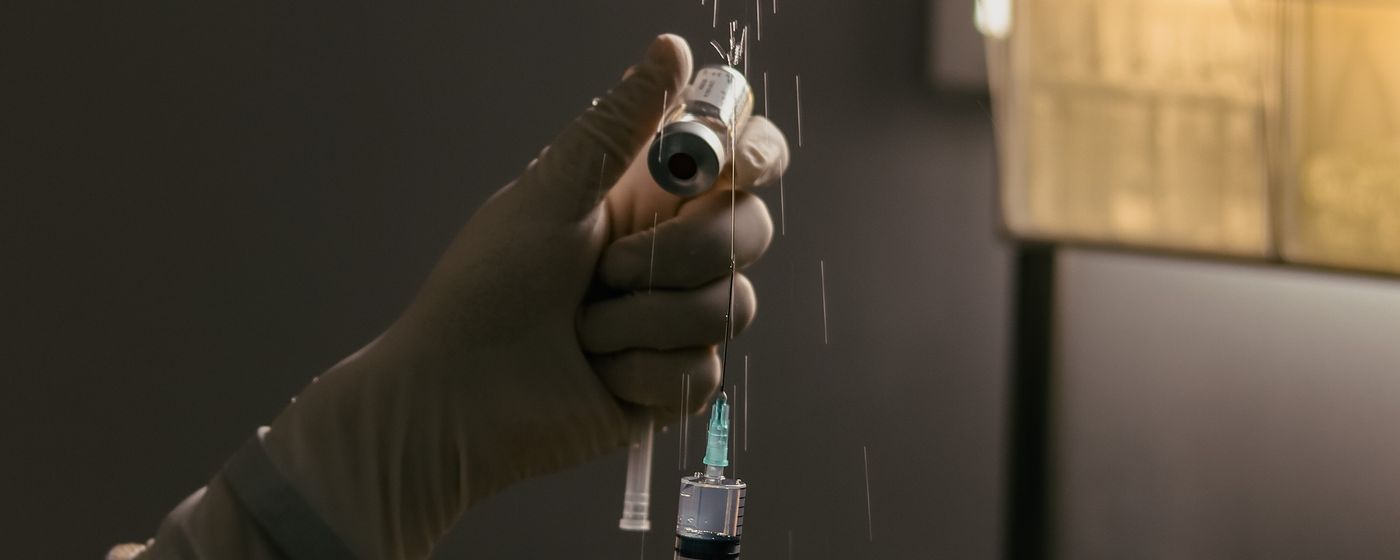 A gloved hand holding a syringe over a laboratory bench