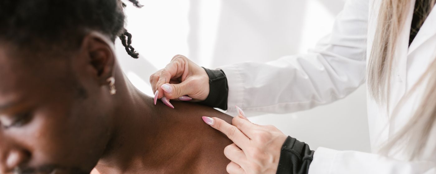 A clinician's gloved hands examining the shoulder and upper back of a seated person