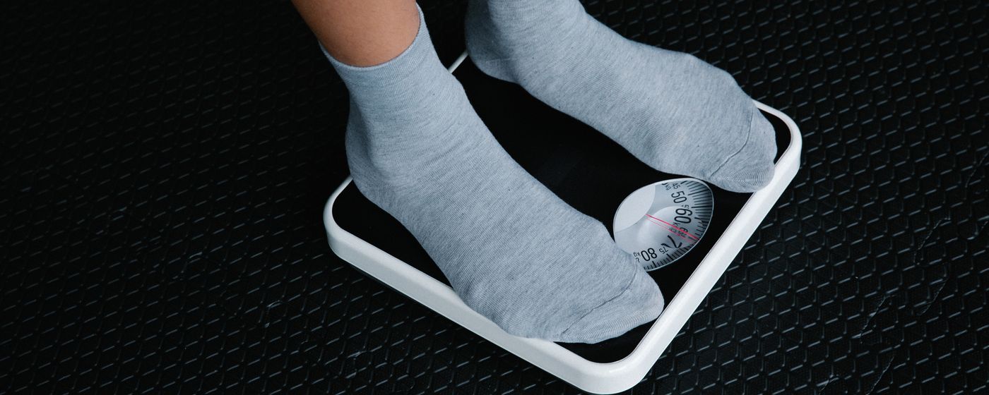 A person's feet in grey socks standing on a dial bathroom scale
