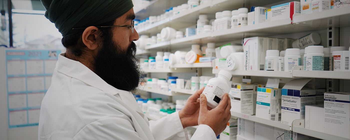 A pharmacist reading the label on a medicine bottle in front of pharmacy shelves