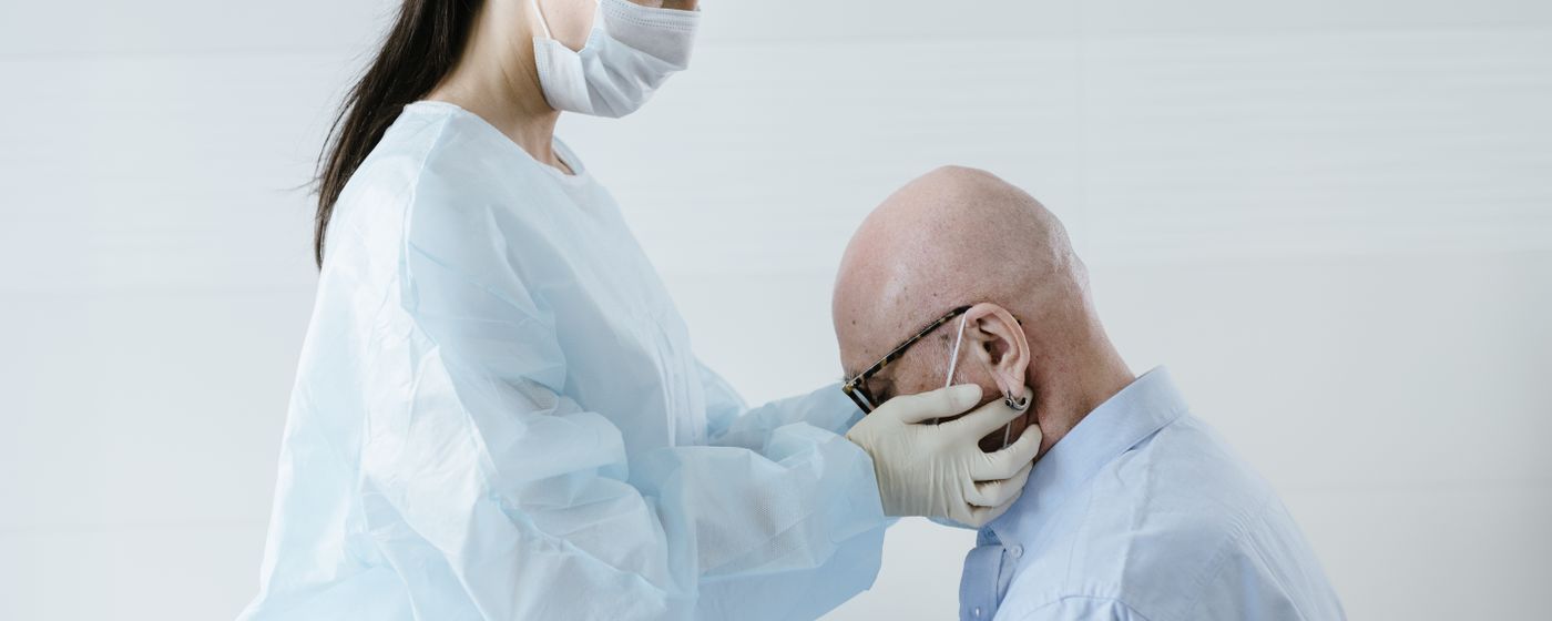 A clinician in gloves examining the side of an older man's face and jaw