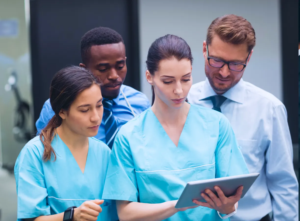 Group of healthcare professionals and a man in a shirt and tie reviewing information on a digital tablet.