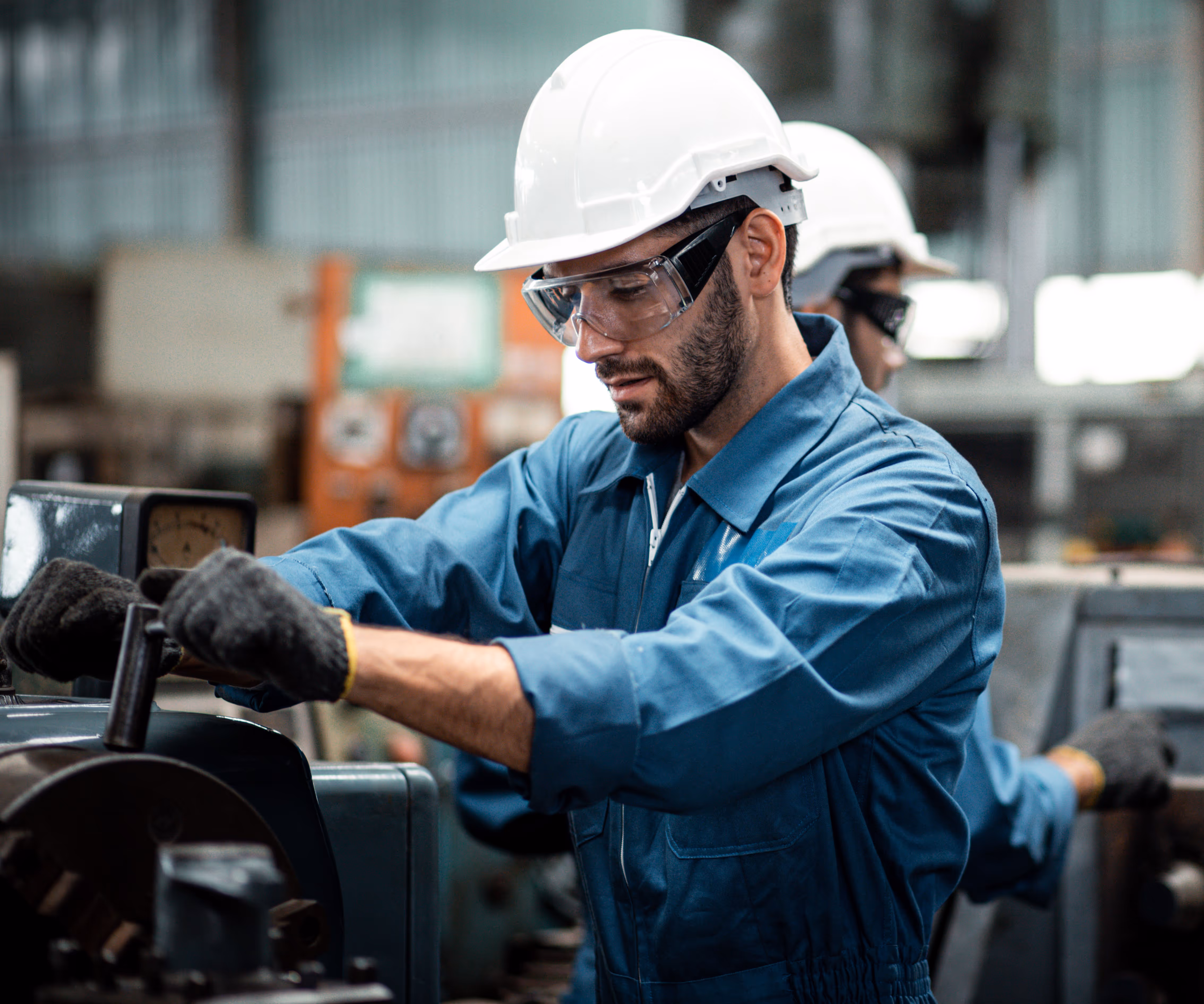 Engineer in a white helmet and safety goggles operating machinery in a factory setting.