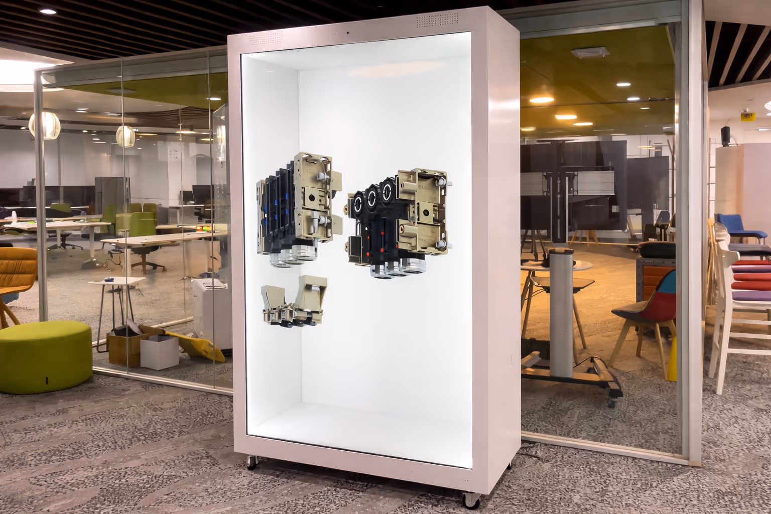 Modern office space with glass walls featuring a large illuminated display case holding mechanical electrical components.