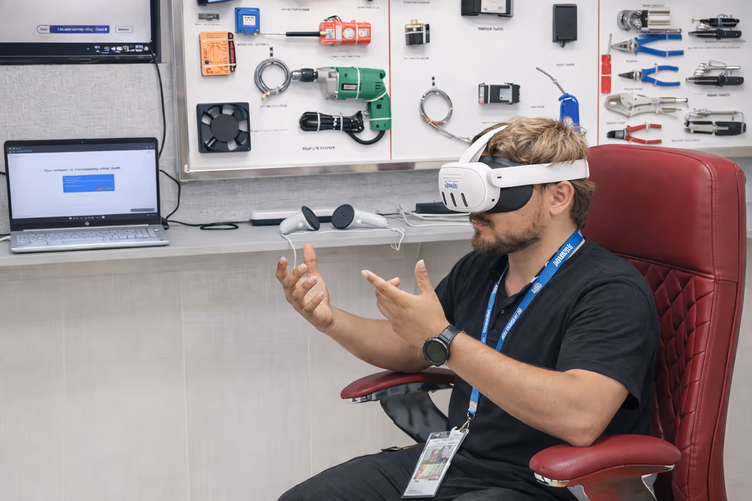 Man seated in a red chair wearing a white virtual reality headset with hands raised, in a room with tools on the wall and a laptop on a shelf nearby.