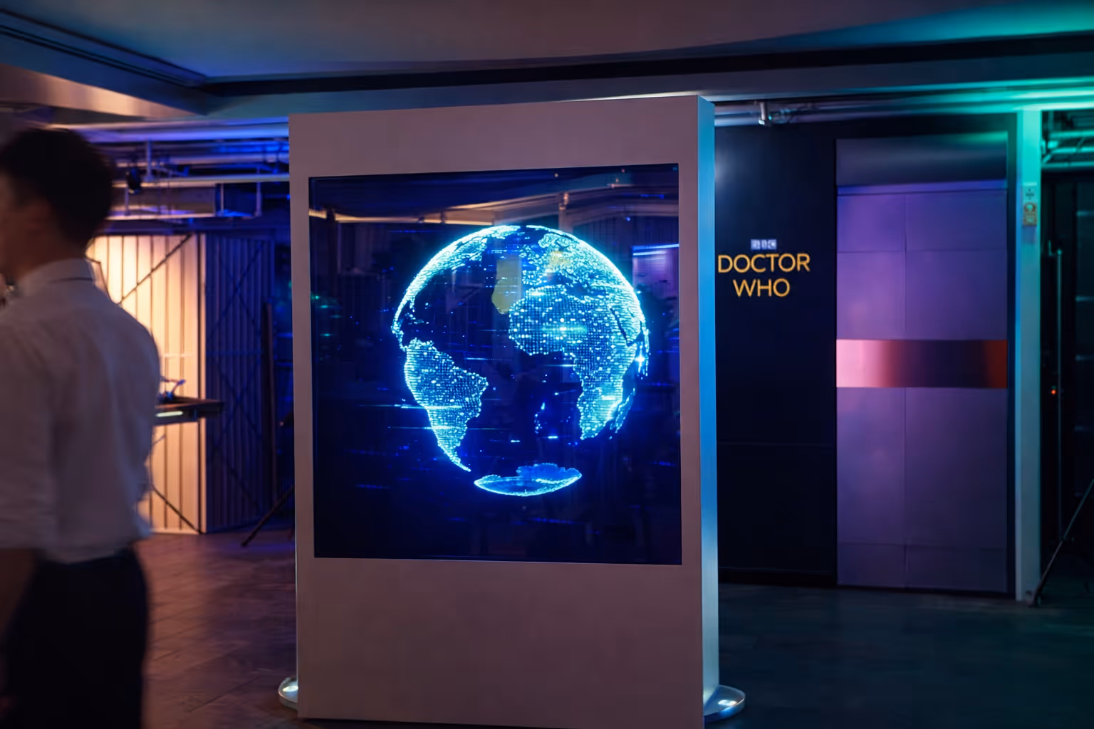 Illuminated digital globe displaying continents in blue lights inside a modern indoor space with 'DOCTOR WHO' sign on the wall.