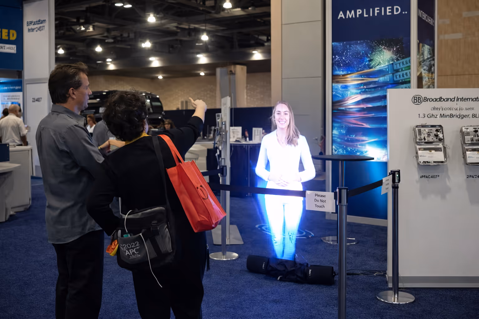 Two people interact with a life-sized hologram of a smiling woman at a technology exhibition.
