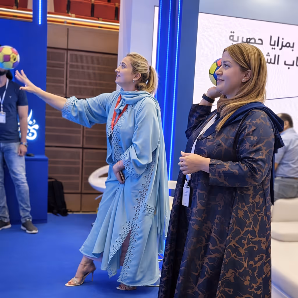 Two women indoors playing with a colourful ball, one preparing to throw and the other holding a ball behind her shoulder.