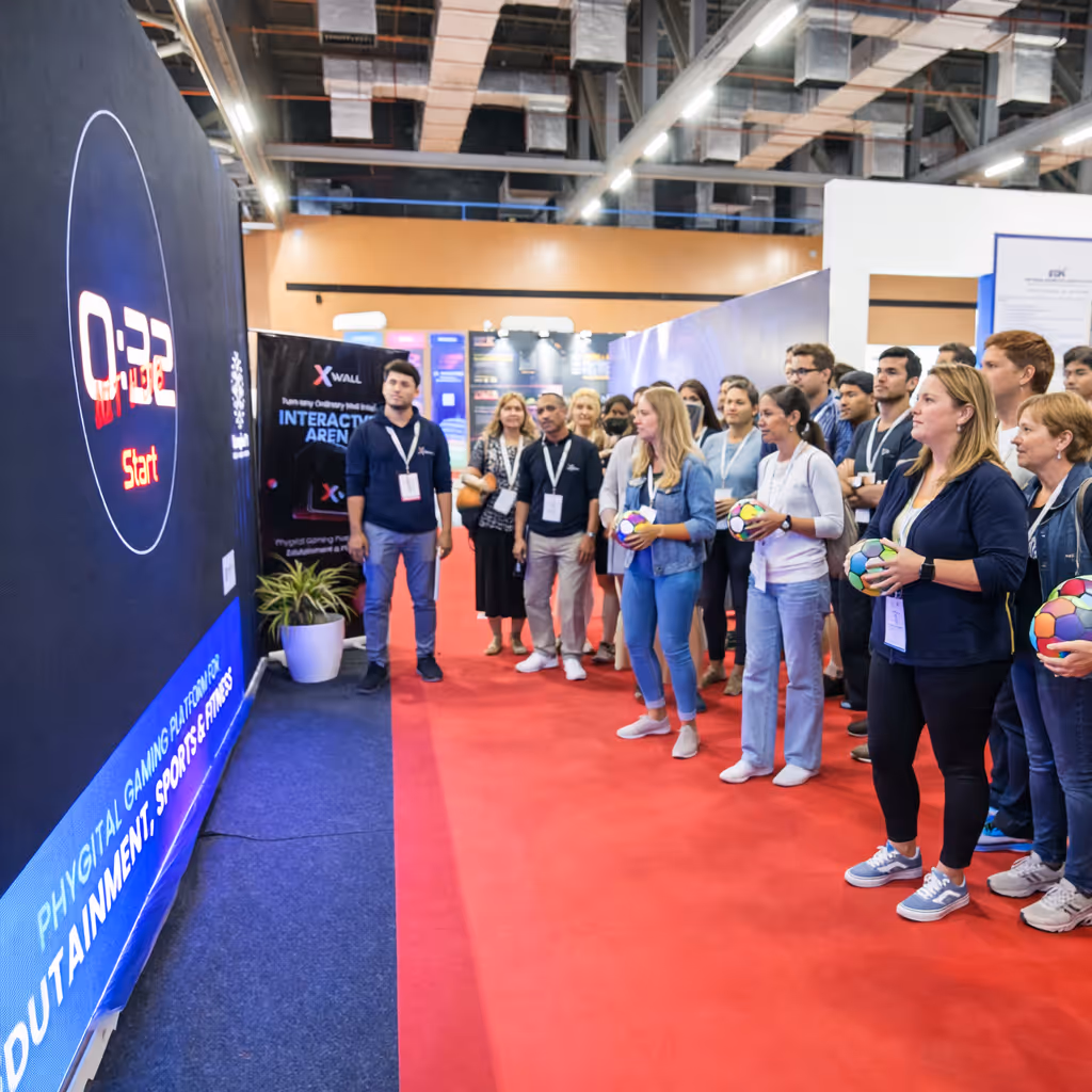 Group of people at an interactive gaming arena event holding colorful balls and watching a large screen with a countdown timer and start button.