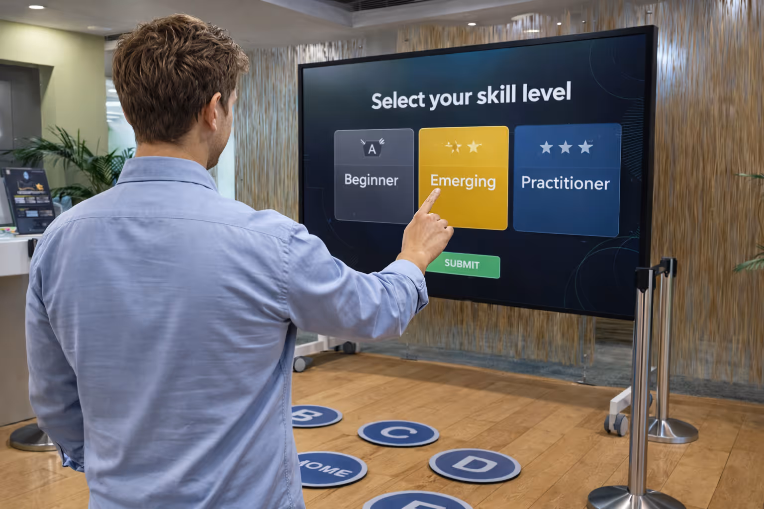 Man in a blue shirt selecting 'Emerging' skill level on a large touchscreen display in an indoor setting.