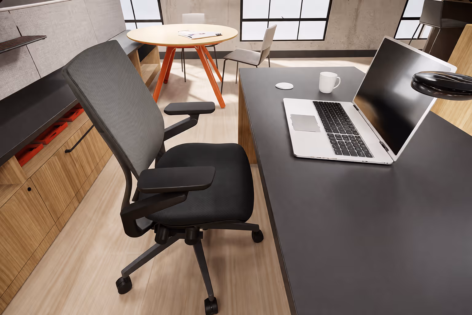 Modern office setup with a black ergonomic chair, laptop, mouse, and coffee mug on a dark desk.